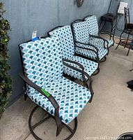 Side view of all four swivel patio chairs with blue and white patterned cushions lined up against a wall.