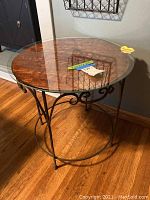 Top view of round table showing wood top covered by clear glass and metal frame with scrollwork