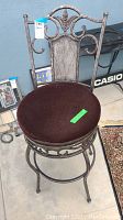 Full view of swivel bar chair showing decorative metal backrest, curved legs, and dark brown cushioned seat.