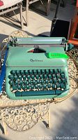 Front view of vintage Optima typewriter on an outdoor table showing its green body and keyboard.