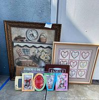 Two large framed wall art pieces and six smaller assorted photo frames arranged on pavement outdoors, showing the family and friend inspirational theme.