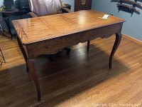 Left front side angle view of the wooden desk showing carved curved legs, scalloped apron, and wood grain surface with scratches.