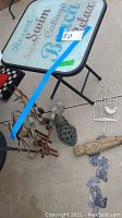 Overview photo showing the small folding table with beach-themed top and the various yard art pieces arranged on the ground including wind chimes, figurines, and decorations.