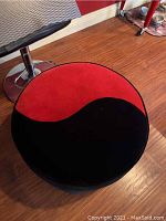 Top view of round ottoman showing yin yang red and black upholstery pattern.