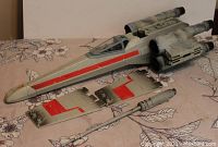Large gray X-Wing Starfighter toy body with detached wings and cockpit canopy. Moderate surface wear visible.