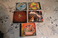 Five PC games laid on floral patterned fabric with discs and boxes visible including Riven, RollerCoaster Tycoon 3, Tonka Search & Rescue and two Ultrahost discs.