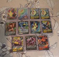 Top view of 11 rare Pokémon cards, individually sleeved lying on a floral cloth surface, showing characters such as Pikachu, Mimikyu, Snorlax, and others.