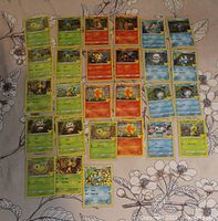 Top-down image showing an assortment of 51 assorted Pokémon cards spread in rows on a floral patterned surface, featuring different Pokémon species with some holographic and foil variations.