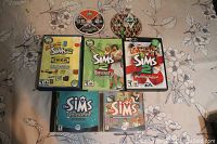 Photo showing six cases and discs of The Sims PC games laid out on floral fabric.