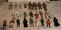 Overview photo showing 25 Star Wars action figures arranged on a floral bedspread, clearly depicting characters including multiple Chewbaccas, Princess Leia figures, a C-3PO, Darth Vader, Luke Skywalker, and others.