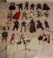 Top view of about 20 Star Wars action figures including humanoid characters, droids, and accessories arranged on floral fabric