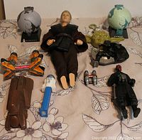 Photo showing the full assortment of Star Wars toys including Anakin Skywalker figure, CORUSCANT and NABOO planet models, Yoda head, Darth Maul figure, R2-D2 toy, jetpack figures, and small accessories.