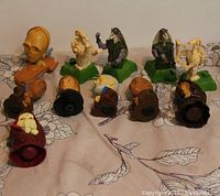 Overview of 11 Star Wars character bust toys arranged in two rows on a cloth surface with leaf pattern. Figures include C-3PO, Jar Jar Binks, battle droids and others.