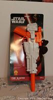 Front view of the Star Wars Finn Blaster toy still in original packaging with white and orange detailing and Star Wars branding.