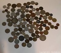 Photo showing a spread of approximately 85 vintage coins of varying sizes, colors, and origins arranged on a white background.