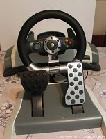 Front view of Xbox 360 steering wheel and pedals showing the black and silver design with rubber grips and colored buttons.