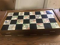Closed folded wooden chessboard with black and painted tiles visible on top with a carved border.