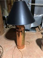 Full view of the copper fire extinguisher lamp with black lampshade on a basement floor.