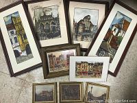 Overview of all nine framed European architectural and landscape paintings on the floor showing varied sizes and styles.