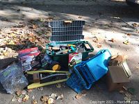 Photo showing the entire lot spread outdoors on ground with fallen leaves. Items include garden cart with tools, hose connector, hose, birdhouse, and stool.