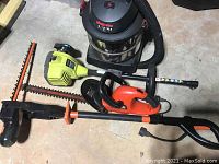 Photo showing the Shop-Vac, Ryobi hedge trimmer, and electric chainsaw placed on the floor.