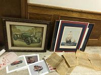 Framed print of a green vintage British sports car with license plate YU 3250, additional vintage car photos, historical documents, and a framed ship artwork in the background.