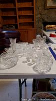 Photo showing the entirety of the crystal lot on the white table with various glassware, decanter, basket, and tray.