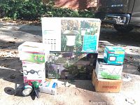 Overview of all lighting items and boxes in the lot placed outdoors on driveway next to vehicle.