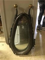 Front view of antique horse collar saddle mirror, showing oval mirror and padded leather frame with brass end caps