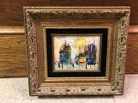 Front view of small framed oil painting with ornate gold frame and black inner liner, showing urban street scene with a bright sun and several figures.