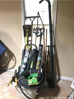 Full view of the lot showing long-handled garden rake, shovel, hose, garden shears and rolled garden mats.