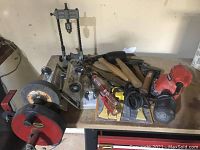 Overview of assorted tools on workbench including drill press stand, sander, hammers, levels, and tapes.