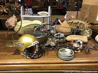 Overall lot viewed on wooden table with multiple items: helmet, stone on stand, metal containers, bicycle figurine