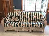 Front view of the vintage wicker sofa with floral striped cushions and matching pillows showing the full length of the sofa and the cushion pattern.