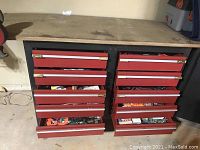 Full view of the metal workbench with six red drawers and open drawers showing some tool and hardware contents.