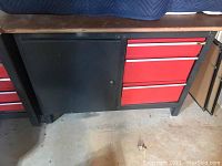 Full view of the metal workbench with wooden top, black cabinet on left, and three red drawers on right.