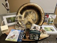Photo of lot items arranged on table showing metal bird bath, Bushnell binocular box, framed bird prints, decorative cranes, book, feeders, birdhouse, ornaments