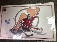 Signed hockey goalie print of Martin Brodeur in red and black New Jersey Devils uniform, posed with glove raised, printed by Cool Ice Images and signed by both Brodeur and artist Sebastien Chabauty.