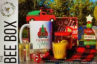 Photo showing contents of the Christmas Bee Box including the mug, honey jar, candle, lip balms, wooden truck ornament, jar opener/coaster, and festive box arrangement