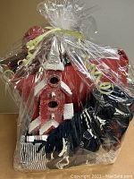 Basket wrapped in cellophane showing two red pillows, a blue blanket, wooden ornament, sign, striped cloth, and ball ornament