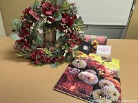 Photo showing Christmas wreath with natural red flowers, pine cones, eucalyptus leaves, accompanying Dahlia May gift certificate and 2022 floral calendar.