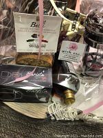 Photo of assorted items in a basket wrapped in clear plastic and pink ribbon, showing biscuits, coffee mugs, coffee press, teas, cloth napkins, wooden cutting boards, decorative bottle, and gift certificate.