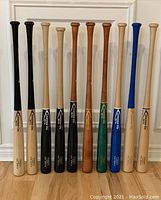 Eleven example bats in various woods and finishes displayed upright against a wall