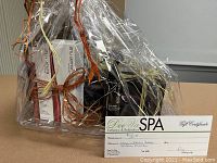 Gift basket wrapped in cellophane containing spa certificate, hair care product boxes, and straightening iron in packaging