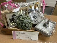 Full view of the gift basket wrapped in clear plastic with pink bows, showing the tray, basket, frames, travel bowls, decorative item, pillow, and gift certificate in front.