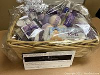 Overview of gift basket contents wrapped in cellophane showing jars, bottles, towel, gift certificate