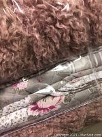 Close-up of folded queen-sized floral quilted blanket and dusty rose curly cushion enclosed in plastic wrapping