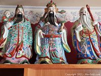 Front view of all three vintage Chinese immortal wise men figurines together on shelf showing detailed colorful hand-painted robes and facial expressions