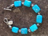 Full view of bracelet showing six rectangular turquoise beads, silver-tone spacer beads, clear round beads, toggle clasp on dark surface