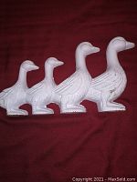 Front view of white cast iron duck doorstop showing connected four ducks in different sizes.
